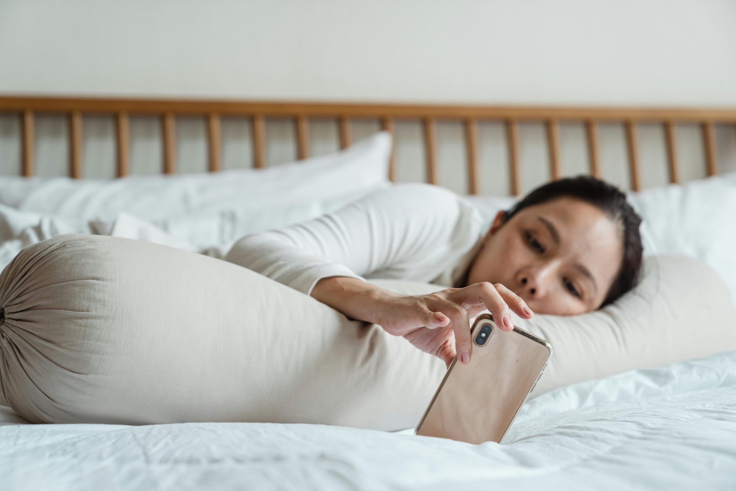 woman laying on bed scrolling on phone